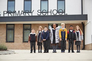 Primary school kids standing in front of their school looking to camera, full length, low angle